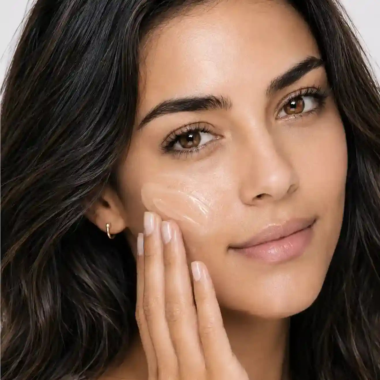 Woman blending Skinara AgeScreen Clear sunscreen into her cheek
