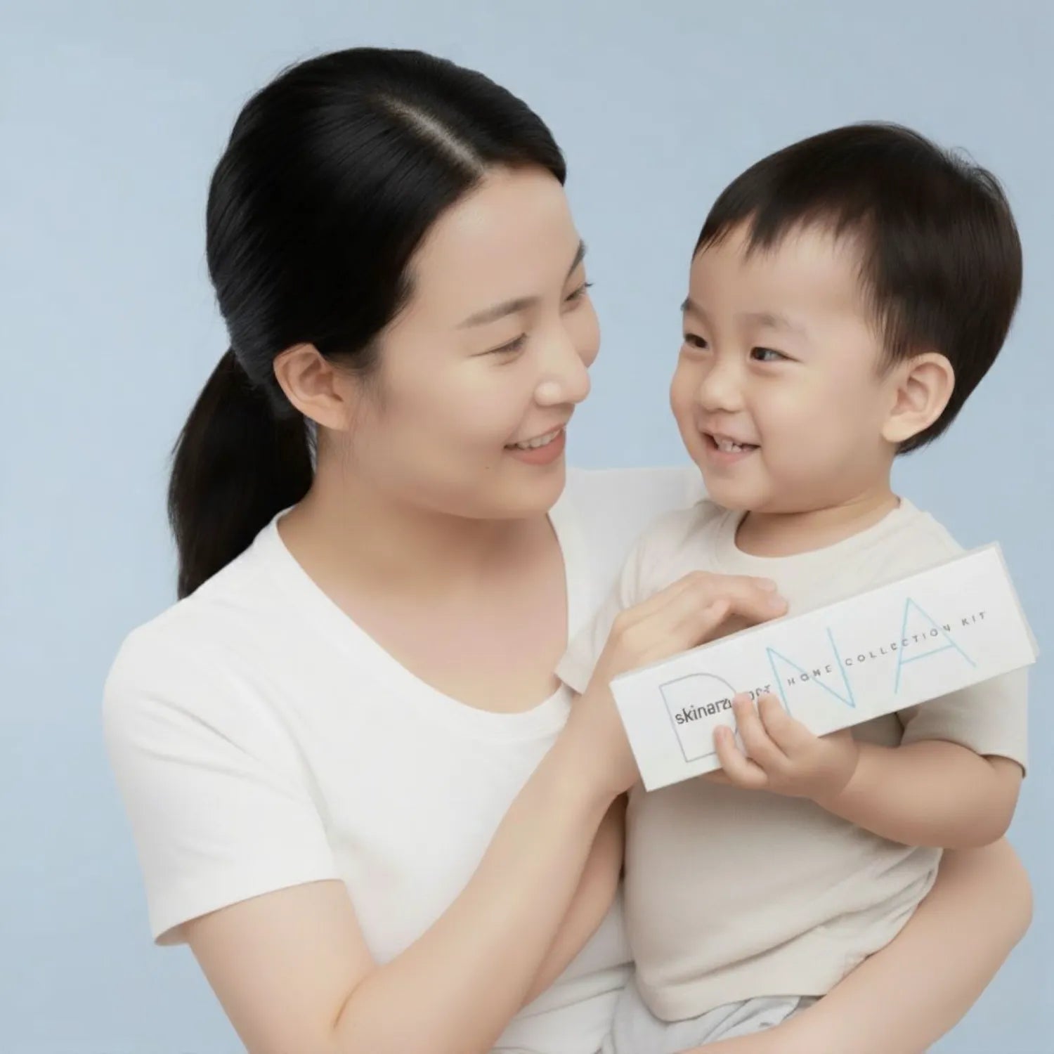 Woman holding a child who is holding a skinara skin DNA testing kit product box against a light blue background
