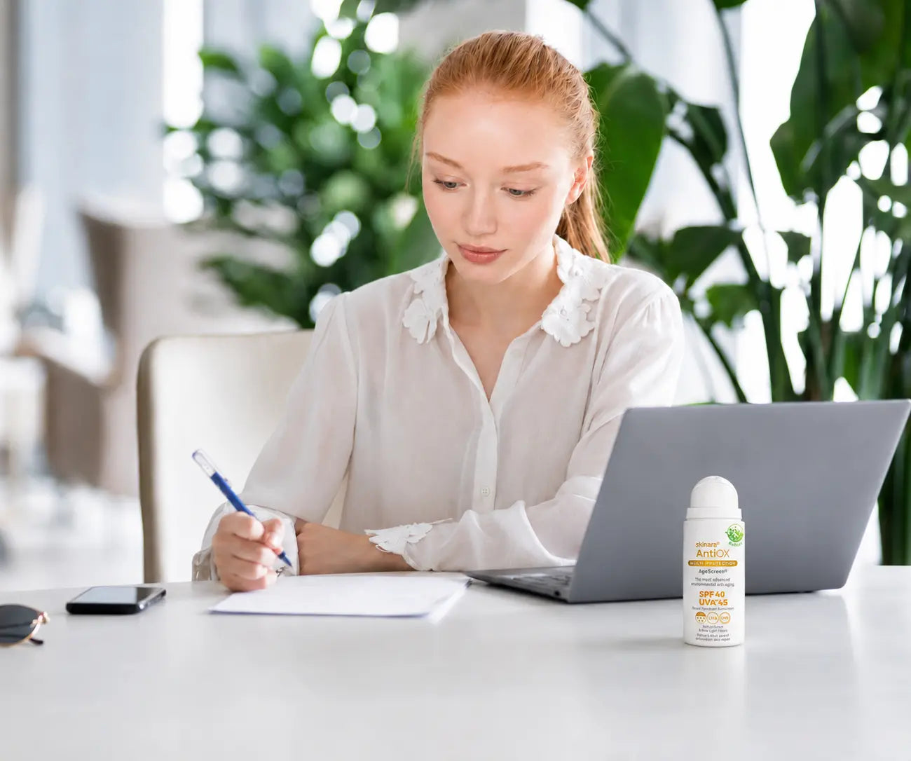 Woman working at a laptop with Skinara AgeScreen sunscreen nearby for daily UVA protection
