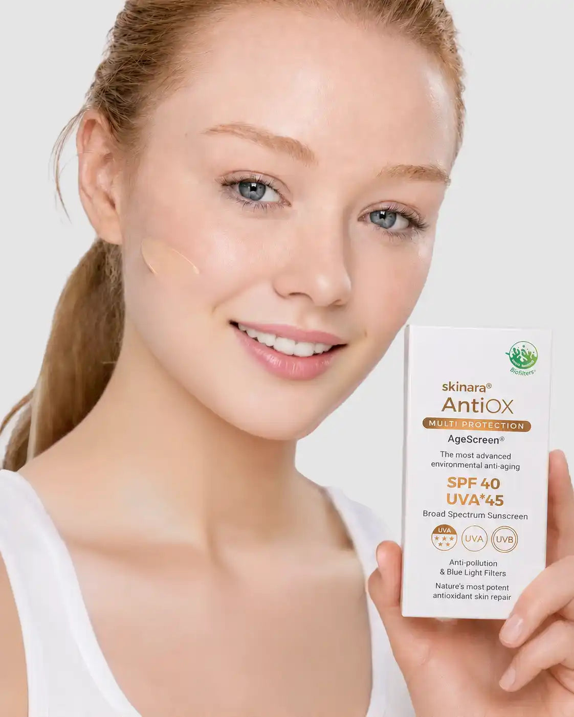 Fair-skinned model wearing Honey Almond AgeScreen tint and holding the sunscreen product